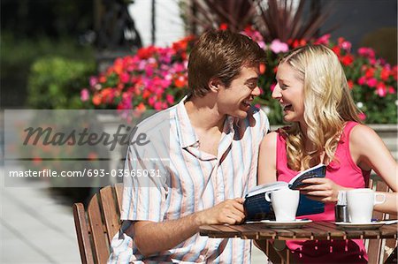 Young couple sitting at outdoor cafe laughing and holding guidebook