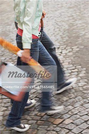 Couple walking, carrying baguette and bags, low section