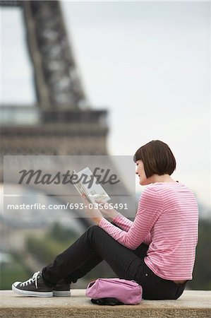France, Paris, Young woman reading book on balcony in front of Eiffel Tower