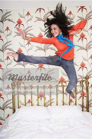 Teenage Girl, arms outspread, kicking, jumping on bed