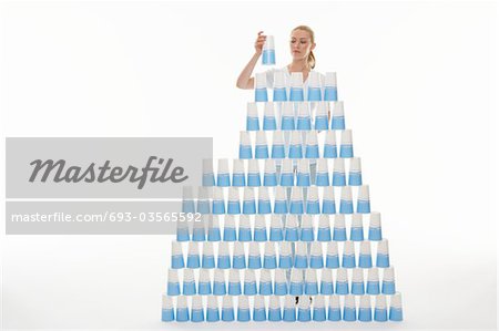 Woman stacking plastic cups into pyramid against white background