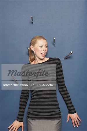 Woman surrounded by thrown knives against blue background