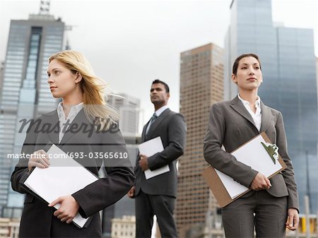 Three business people with clipboards outside office buildings