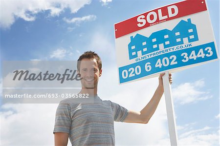 Man holding sold sign, against sky