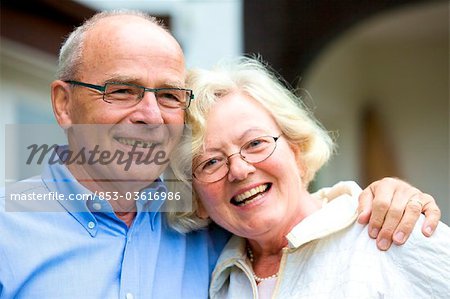 Happy senior couple embracing in front of residential building, portrait