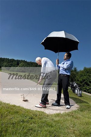 Caddy is holding a parasol over a golfer