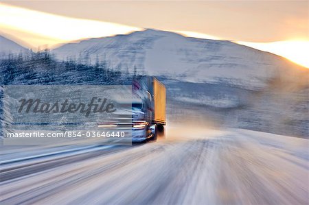 Semi truck driving on the snowcovered Seward Highway at sunrise, Southcentral Alaska, Winter