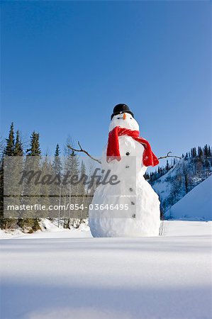 Bonhomme de neige avec une écharpe rouge et un chapeau haut de forme noir assis à côté d'une neige a couvert le lit de rivière, centre-sud de l'Alaska, hiver