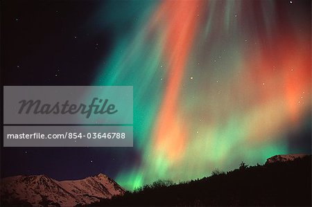 Multi colored Northern Lghts (Aurora borealis) fill the night sky and cast colored shadows on the mountain tops of Chugach State Park, Southcentral Alaska, Winter