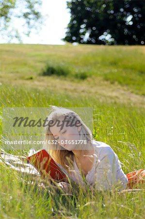 Young woman lying on ground reading book