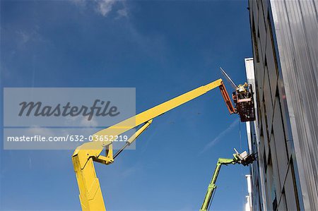 Construction workers in cherry picker bucket working on building exterior