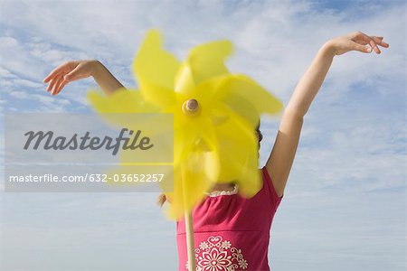 Jeune fille debout à l'extérieur avec bras soulevé, visage masqué par pinwheel en avant-plan