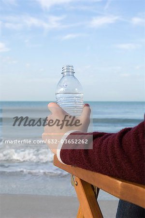 Person sitzt Wasser relaxen am Strand, Flasche in der hand
