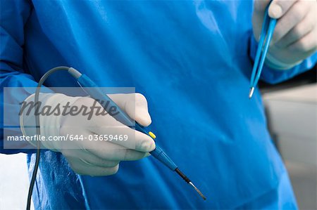 Hands holding electrical surgical scalpel and tweezers in operating room