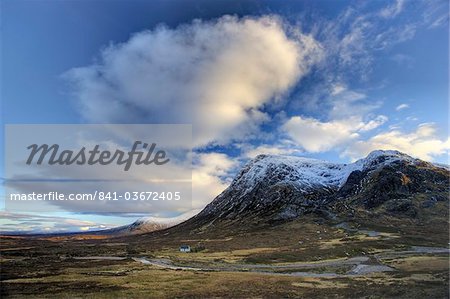 Vue hivernale de Rannoch Moor montrant lone cottage blanchi à la chaux sur la berge d'une rivière, éclipsée par les montagnes couvertes de neige et ciel de soirée dramatique, Rannoch Moor, près de Fort William, Highland, Ecosse, Royaume-Uni, Europe