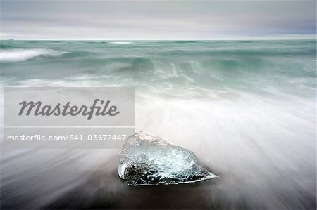 Piece of glacial ice washed ashore by the incoming tide onto beach of volcanic sand near glacial lagoon at Jokulsarlon, Iceland, Polar Regions