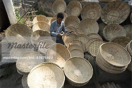 Basketmaker lire le journal en attendant pour les clients au marché tôt le matin sur les rives du Brahmapoutre rivière, Guwahati, Assam, Inde, Asie