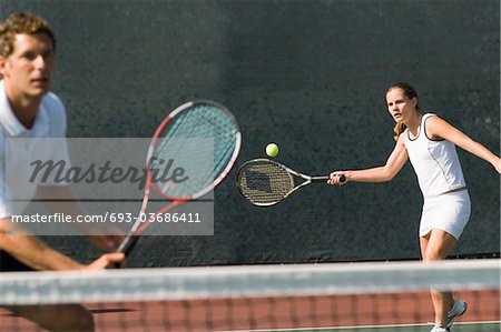 Mixed Doubles player hitting tennis ball, partner standing near net