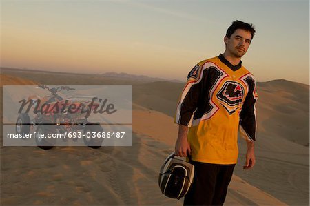 Man standing by quad bike in desert at sunset