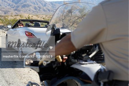 Police officer on motorbike stopping car on desert road side