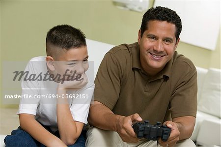 Sohn mit Vater Playing Video-Spiel auf Sofa im Wohnzimmer