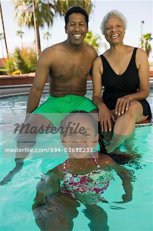 Girl (5-6) with father and grandmother at swimming pool, portrait.