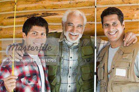 Homme d'âge mûr avec deux fils tenant des cannes à pêche, souriant, (portrait)