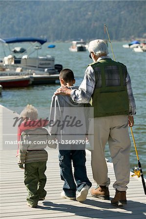 Grand-père et deux petits-fils détenant des cannes à pêche, marchant sur la jetée, vue arrière