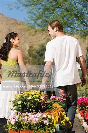 Young couple pulling cart with potted flowers in garden centre, rear view