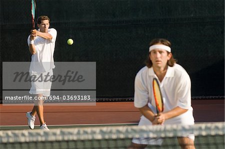 Joueuse de tennis frappe revers ; partenaire de double accroupi au net
