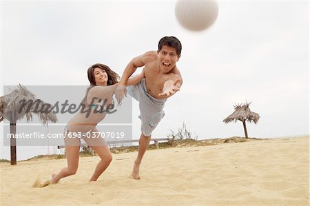 Woman Holding Man Back from Diving for Volleyball on Beach