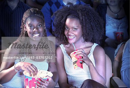 Amis souriants assis dans le théâtre avec pop-corn et soude, regarder film