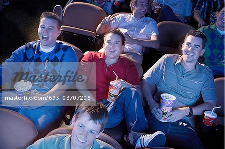 Young men reclining, watching movie in theatre, smiling