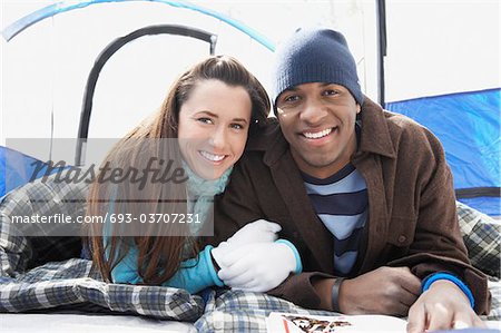 Jeune couple se trouvant dans des sacs de couchage sous tente, portrait.