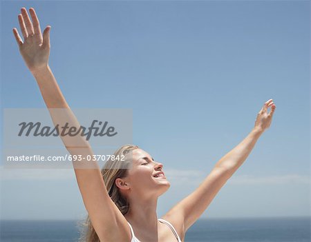 Jeune femme avec les bras tendus et les yeux fermés sur la plage