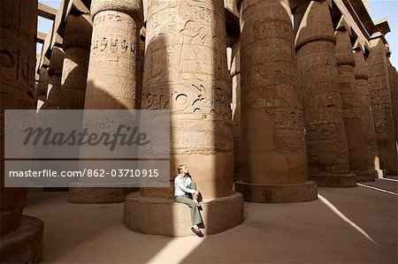 Ägypten, Karnak. Ein Tourist sitzt an der Basis einer massiven steinernen Spalte in die große Hypostyle-Halle.