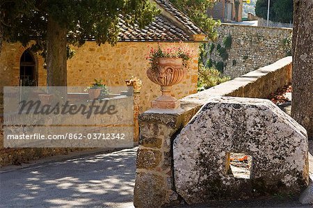 Italie, Toscane, Petroio. Une meule et cache-pots en terre cuite décorent le bord d'une route tranquille dans le village de Petroio.