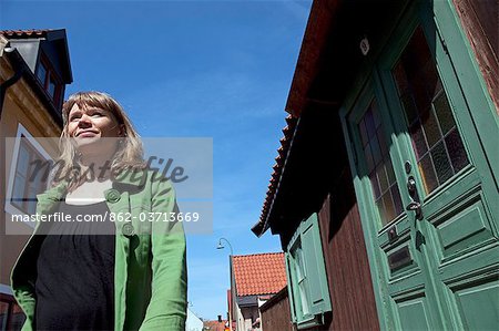 Sweden, Island of Gotland, Visby. A Tourist strolls past the traditional timber built houses of an old-style area.