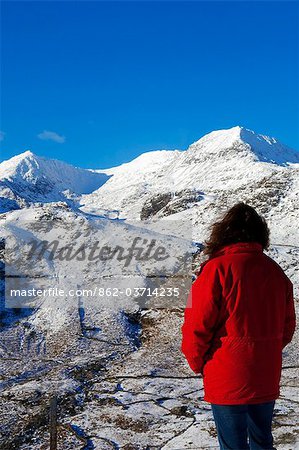 Wales, Gwynedd, Snowdonia. A walker looks westwards to the snow covered slopes of Snowdon.