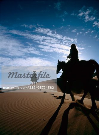 Horseback riders in silhouette on sand dune