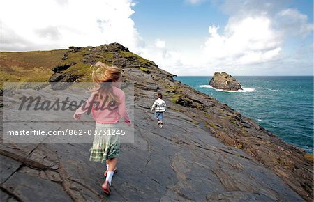 England, Cornwall. A boy and a girl walk along clifftops towards Penally Point at Boscastle.
