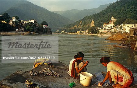 India, Uttarakhand, Rishikesh. Villagers wash clothes by the River Ganges against a backdrop of wooded hill.