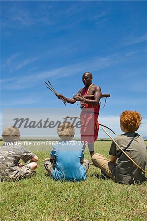 Kenya, Masai Mara. Safari guide, Salaash Ole Morompi, shows different tips on his Maasai arrows to boys on safari.