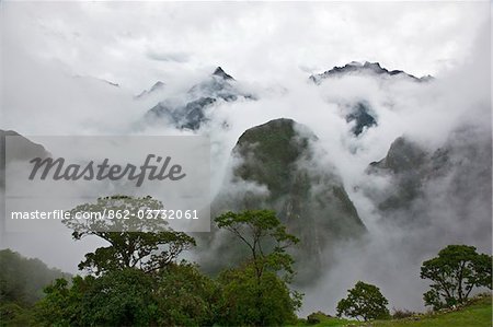 Peru, In the early morning, low mist and clouds rise from the steep-sided valleys surrounding the Inca ruins at Machu Picchu.