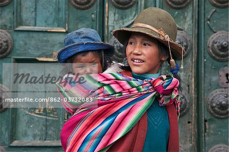 Au Pérou, une jeune fille péruvienne porte sa petite sœur sur son dos à côté des portes massives églises de Iglesia de la Compania de Jesus dans s Cusco Plaza de Armas.