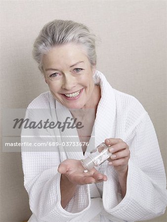 Smiling senior woman wearing bathrobe holding medicine