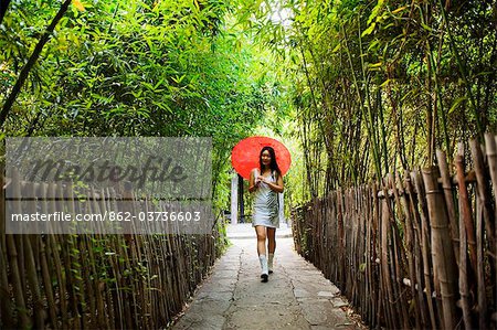 China, Beijing, Ethnic Minorities Park, a girl with parasol walking through a bamboo grove