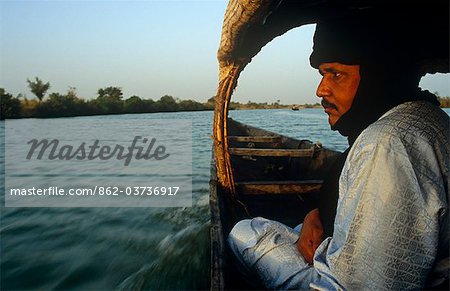Mali. near Segou, Kalabougou. A Tuareg guide sits in a small boat, or pirogue, crossing the River Niger at Kalabougou.