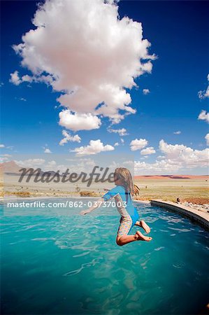 Sossusvlei Mountain Lodge, Namib Rand Nature Reserve, Namibia. A girl jumps into the pool with views towards the Desert.