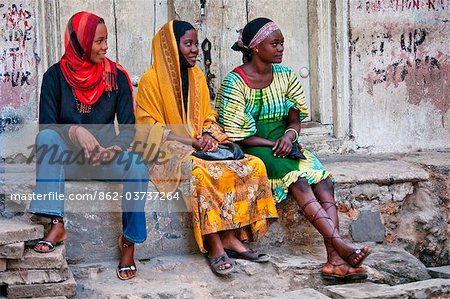 Tanzanie, Zanzibar, Stone Town. Trois jeunes femmes se détendre sur une étape de pierre à Stone Town.